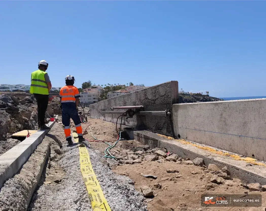 Operarios junto a una sierra sobre carril instalada en un muro costero.