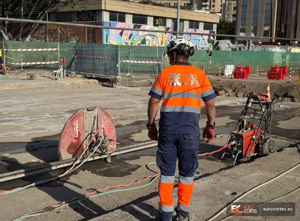 Operario con uniforme de Eurocortes junto a una sierra de disco en una obra exterior.