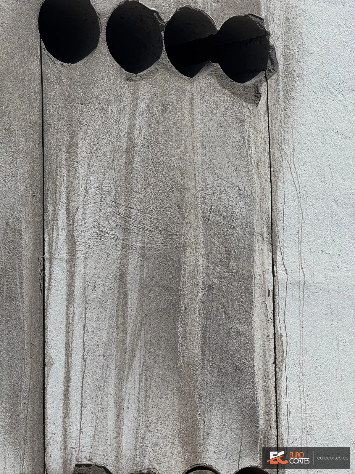 Primer plano de una batería de perforaciones con corona en un muro de hormigón.