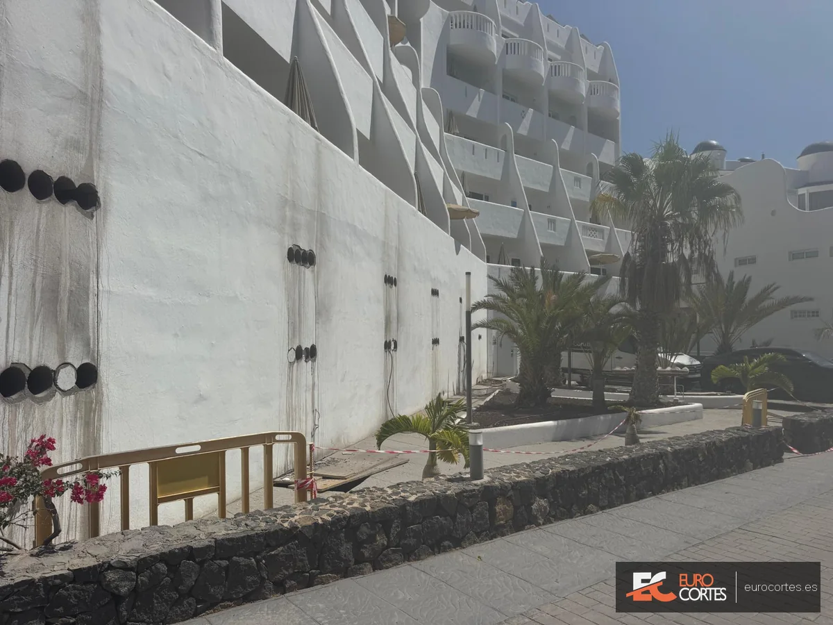 Zona de obra acordonada ante un muro con varias perforaciones para paso de instalaciones.
