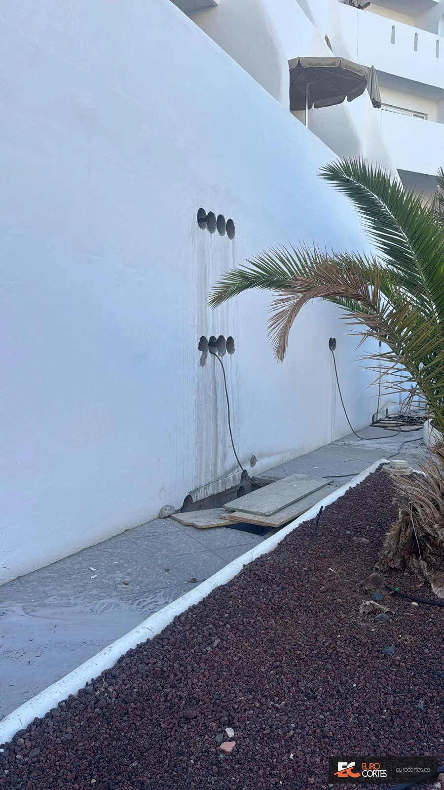 Perforaciones con corona y cableado junto a una zona ajardinada.