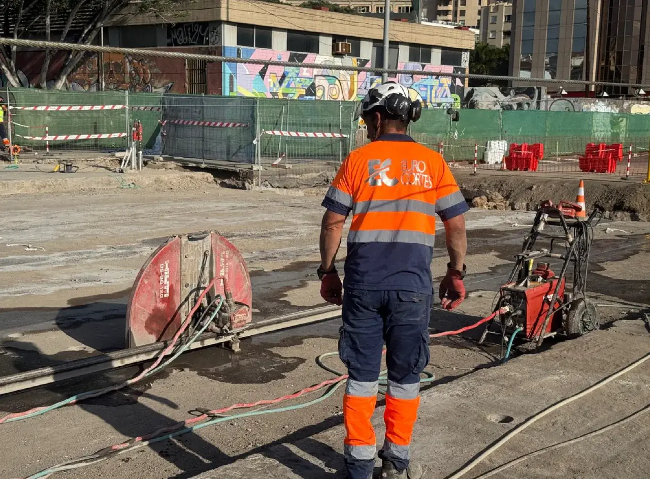 Operario con uniforme de Eurocortes junto a una sierra de disco en una obra exterior.