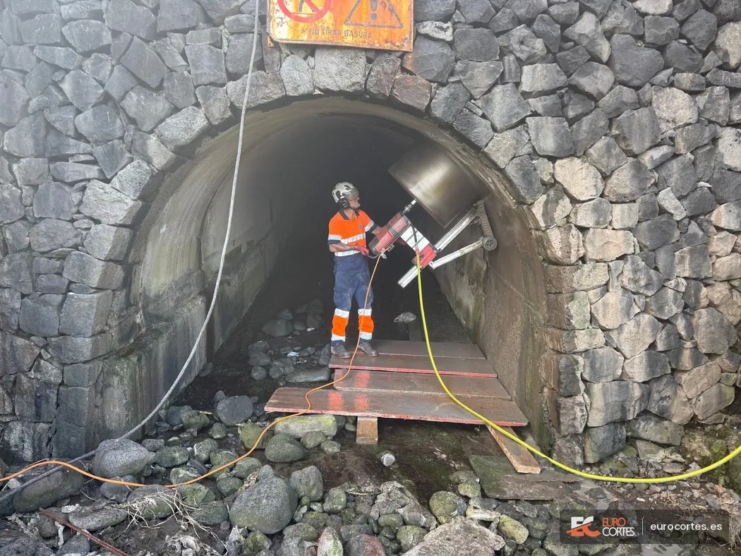 Operario perforando con corona de gran diámetro la bóveda de un túnel de piedra.
